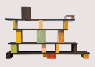 A modern, multicolored bookshelf by Alfredo Quiroz features staggered shelves and vertical supports in various colors and textures, showcasing open spaces and a minimalist design.