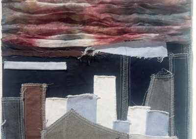 A textile artwork by Alfredo Quiroz depicts a cityscape with abstract buildings in neutral tones and layered, sheer fabric clouds in shades of red, brown, and gray above, creating a dramatic, textured sky.