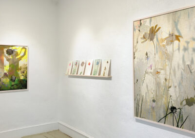 A gallery wall at El Zaguán displays two large botanical-themed artworks by Elizabeth Chiles and six smaller pieces in a row, all featuring soft, nature-inspired imagery with flowers in light, muted tones for 2025.