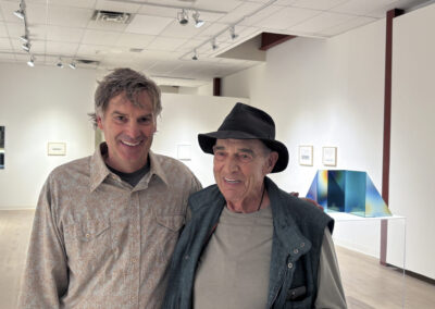 Two men smiling and standing together in a bright, modern art gallery with white walls and contemporary artwork displayed in the background at Bell Mills 2025.