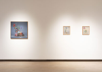 A gallery wall displaying three framed floral artworks—one large 2025 McConville painting of a detailed flower arrangement on the left, and two smaller, more minimal Munroe floral paintings on the right, all set against a plain white background.