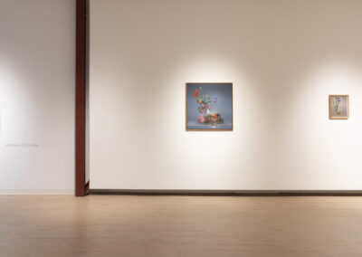 A gallery wall displays five framed artworks by Munroe and McConville featuring floral and botanical themes, spaced evenly on a white wall with wooden flooring and overhead lighting highlighting each piece—a 2025 showcase of artistic elegance.