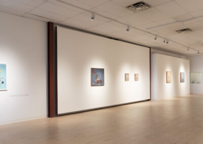 A spacious art gallery with light wood floors and white walls displays colorful, floral-themed artworks by Munroe. Track lighting highlights each piece, creating a calm and modern setting for the 2025 McConville exhibit.