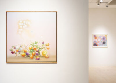 A framed Munroe painting of colorful fruits on a soft pink background hangs on a white gallery wall; another abstract McConville artwork with circular patterns is visible in the brightly lit 2025 gallery room.