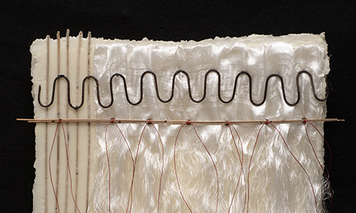 A mixed-media artwork featuring white rods on the left, a wavy black line across sheer white fabric, thin red threads hanging down, and a horizontal wooden stick, all set against a black background.