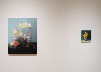 Two abstract floral paintings hang on a plain white wall. The left painting is larger and features white and yellow flowers with dark accents, while the smaller painting on the right shows a colorful bouquet in a vase.