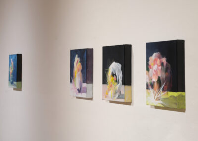 Four abstract floral paintings are displayed in a row on a white wall. Each canvas features colorful, blurred flower arrangements with dark backgrounds and soft bold brushstrokes.