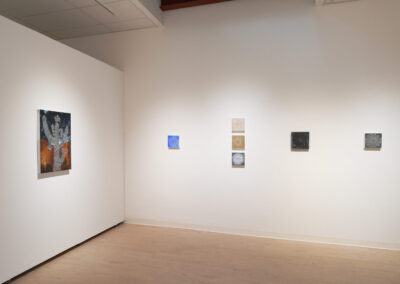 A minimal art gallery with six small, abstract paintings arranged in a row on a white wall, with another abstract painting displayed on the adjacent wall; light wood floor and bright overhead lighting.