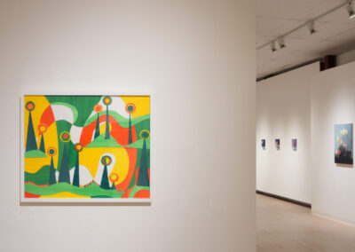 Colorful abstract painting with green, yellow, orange, and red shapes and circles hangs on a white gallery wall; more artwork is visible in the background along a well-lit hallway.