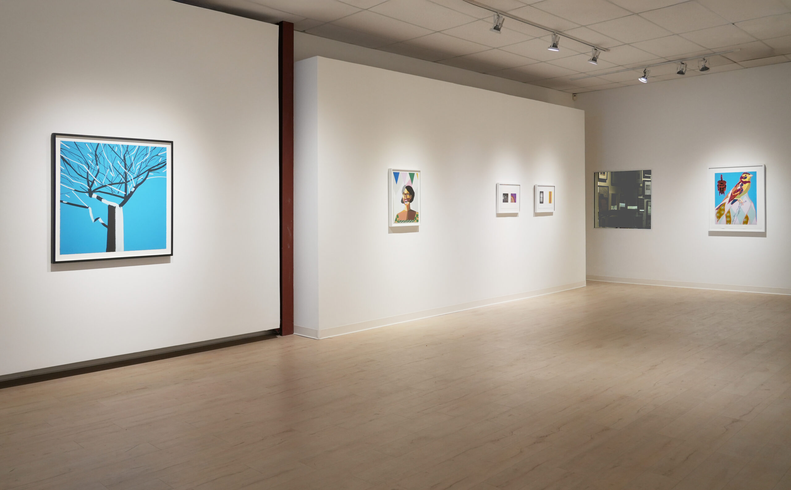 A contemporary art gallery with white walls and light wooden flooring features various abstract artworks. The space includes a pair of blue armchairs and a round wooden table in the foreground, with more art displayed in the background and along the walls.