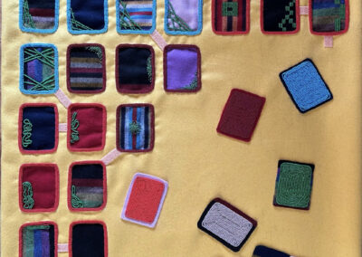 A grid of colorful embroidered fabric squares is arranged on a yellow surface, with some squares set aside in scattered piles at the bottom right.
